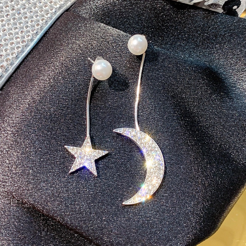 Asymmetric earrings featuring moon and star designs, adorned with pearls and rhinestones, showcasing a celestial theme.