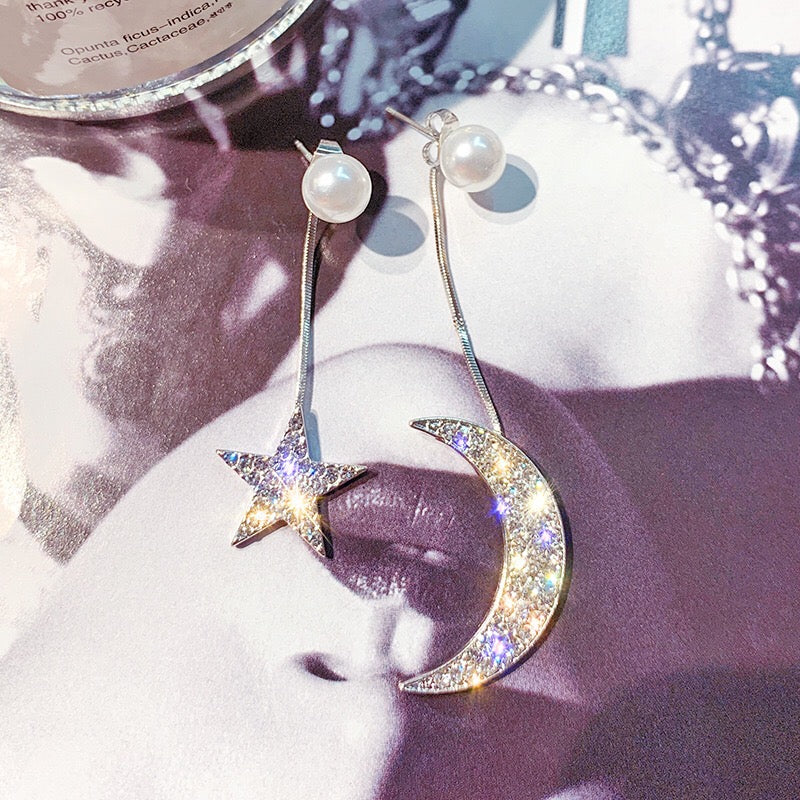 Asymmetric earrings featuring moon and star designs, adorned with pearls and rhinestones, showcasing a celestial theme.