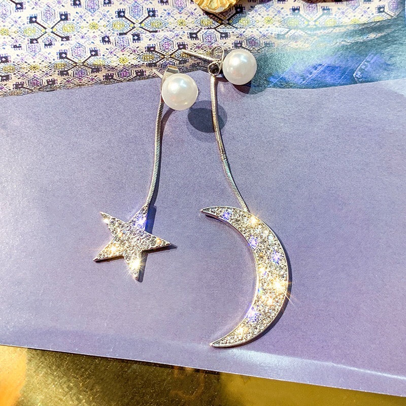 Asymmetric earrings featuring moon and star designs, adorned with pearls and rhinestones, showcasing a celestial theme.