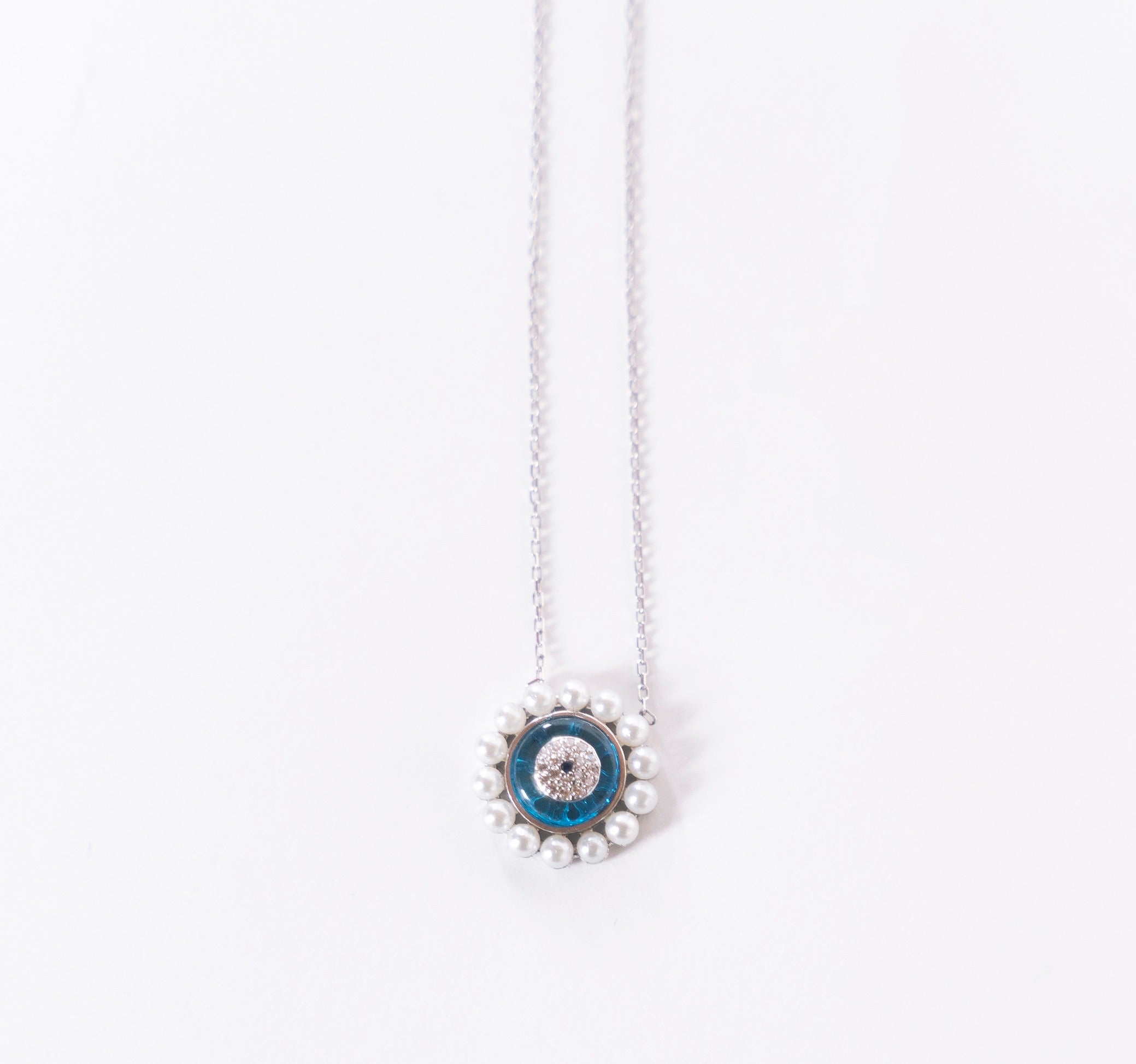 AYRA Necklace featuring mini pearls, evil eye pendant, sea-blue enamel, and cubic zirconia accents on a silver chain.