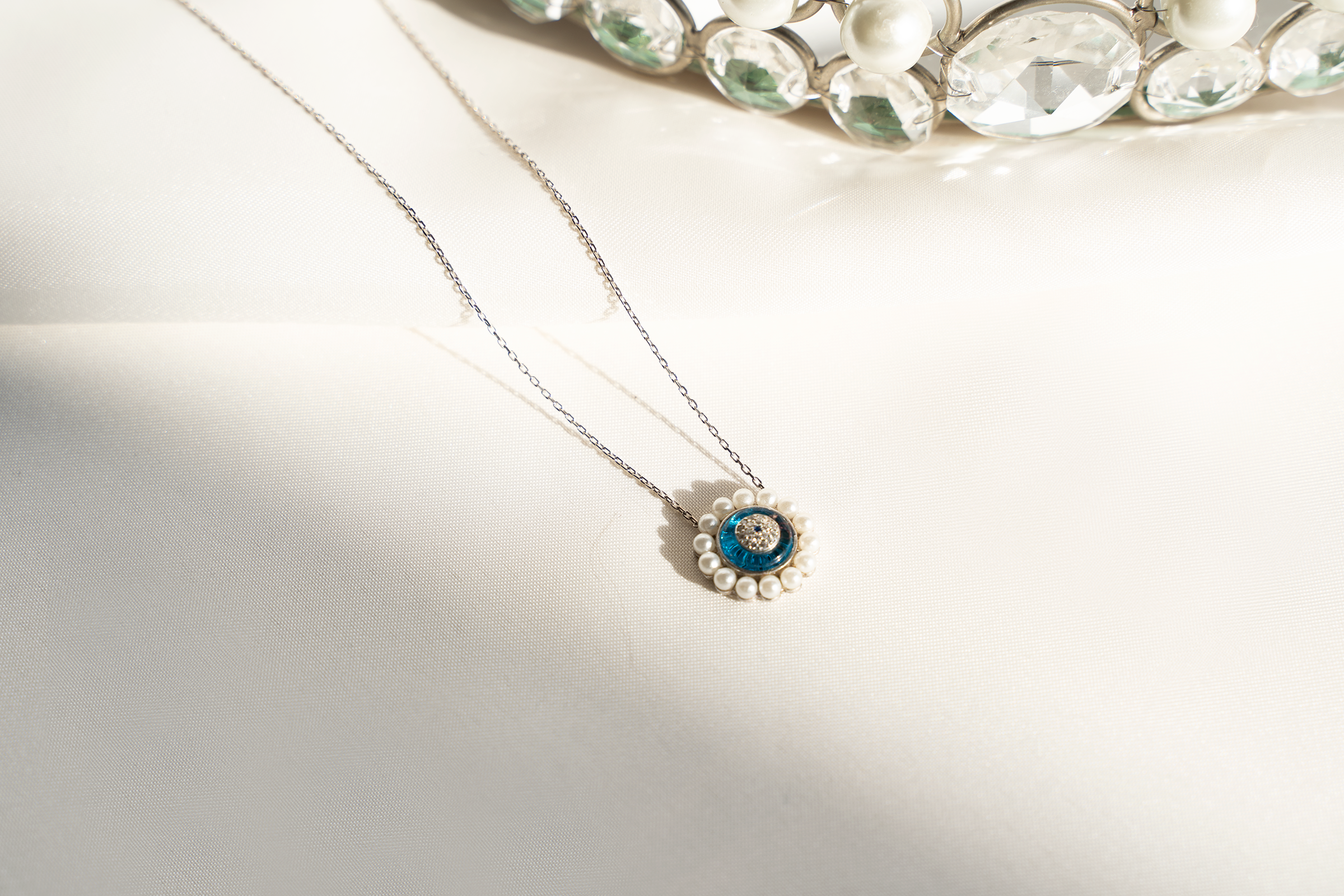 AYRA Necklace featuring mini pearls, evil eye pendant, sea-blue enamel, and cubic zirconia accents on a silver chain.