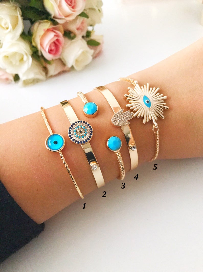 Handmade blue evil eye bangle bracelet with gold accents, featuring an adjustable design and multiple style options.