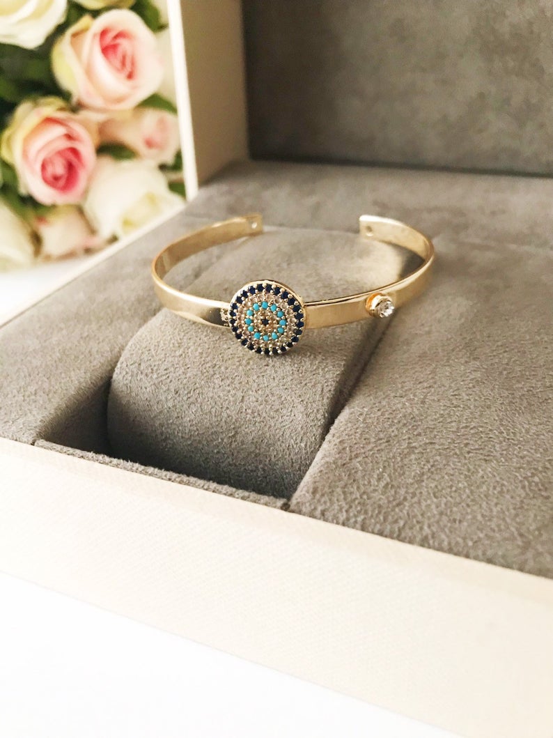 Handmade blue evil eye bangle bracelet with gold accents, featuring an adjustable design and multiple style options.