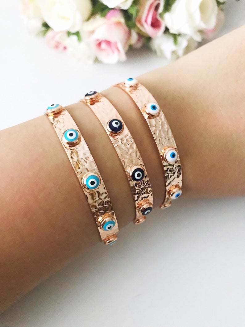 A stunning Evil Eye Bangle Bracelet featuring a movable oval charm, available in rose gold and silver finishes with customizable bead colors.