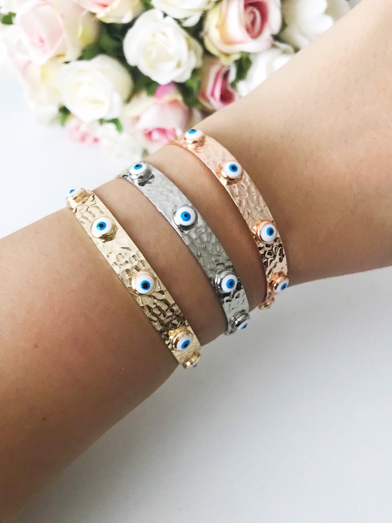 A stunning Evil Eye Bangle Bracelet featuring a movable oval charm, available in rose gold and silver finishes with customizable bead colors.