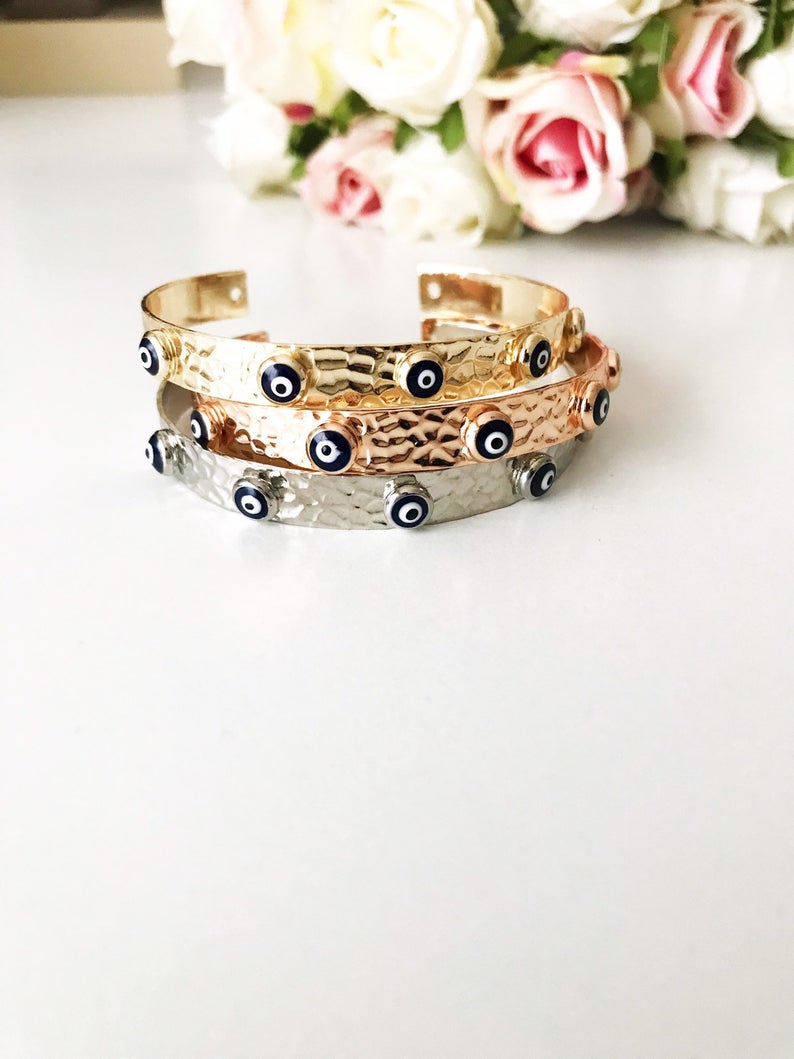 A stunning Evil Eye Bangle Bracelet featuring a movable oval charm, available in rose gold and silver finishes with customizable bead colors.