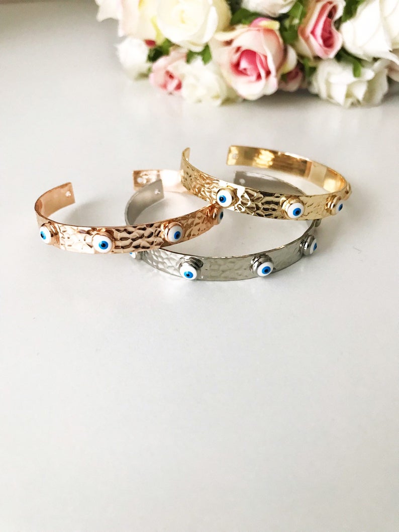 A stunning Evil Eye Bangle Bracelet featuring a movable oval charm, available in rose gold and silver finishes with customizable bead colors.