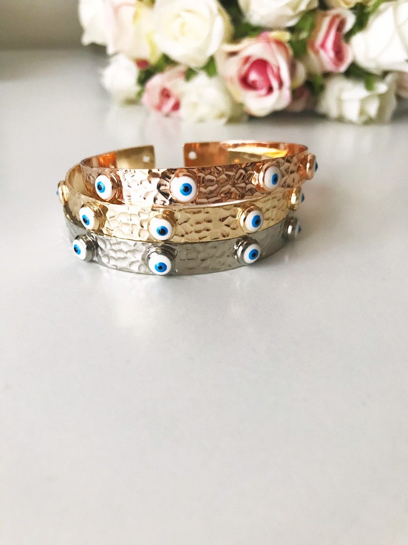 A stunning Evil Eye Bangle Bracelet featuring a movable oval charm, available in rose gold and silver finishes with customizable bead colors.