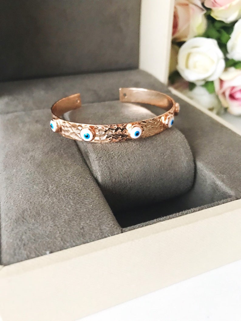 A stunning Evil Eye Bangle Bracelet featuring a movable oval charm, available in rose gold and silver finishes with customizable bead colors.