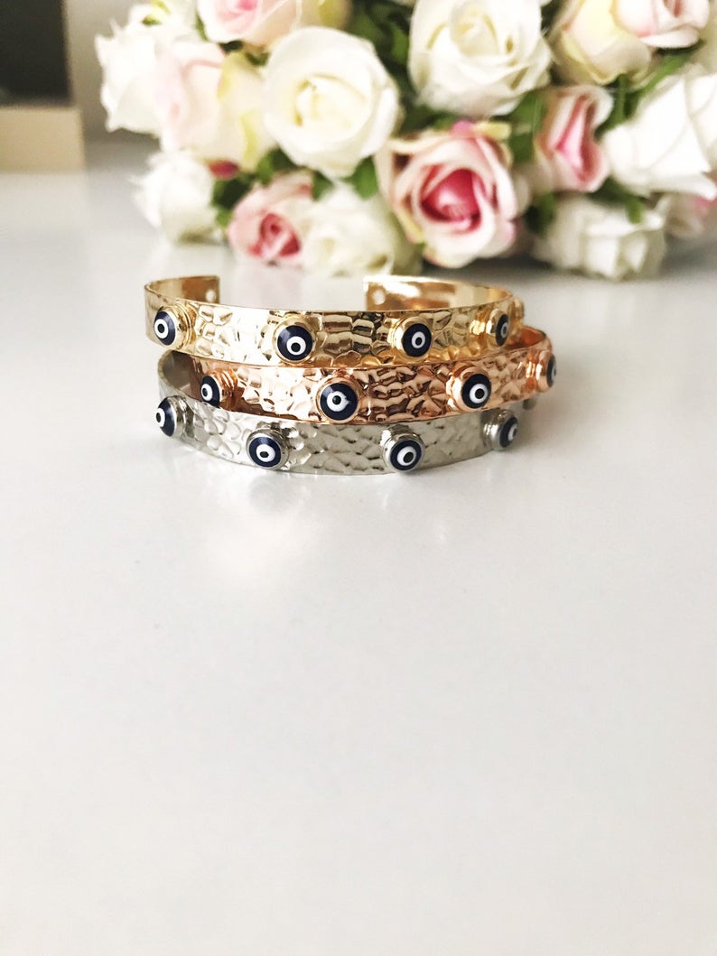 A stunning Evil Eye Bangle Bracelet featuring a movable oval charm, available in rose gold and silver finishes with customizable bead colors.