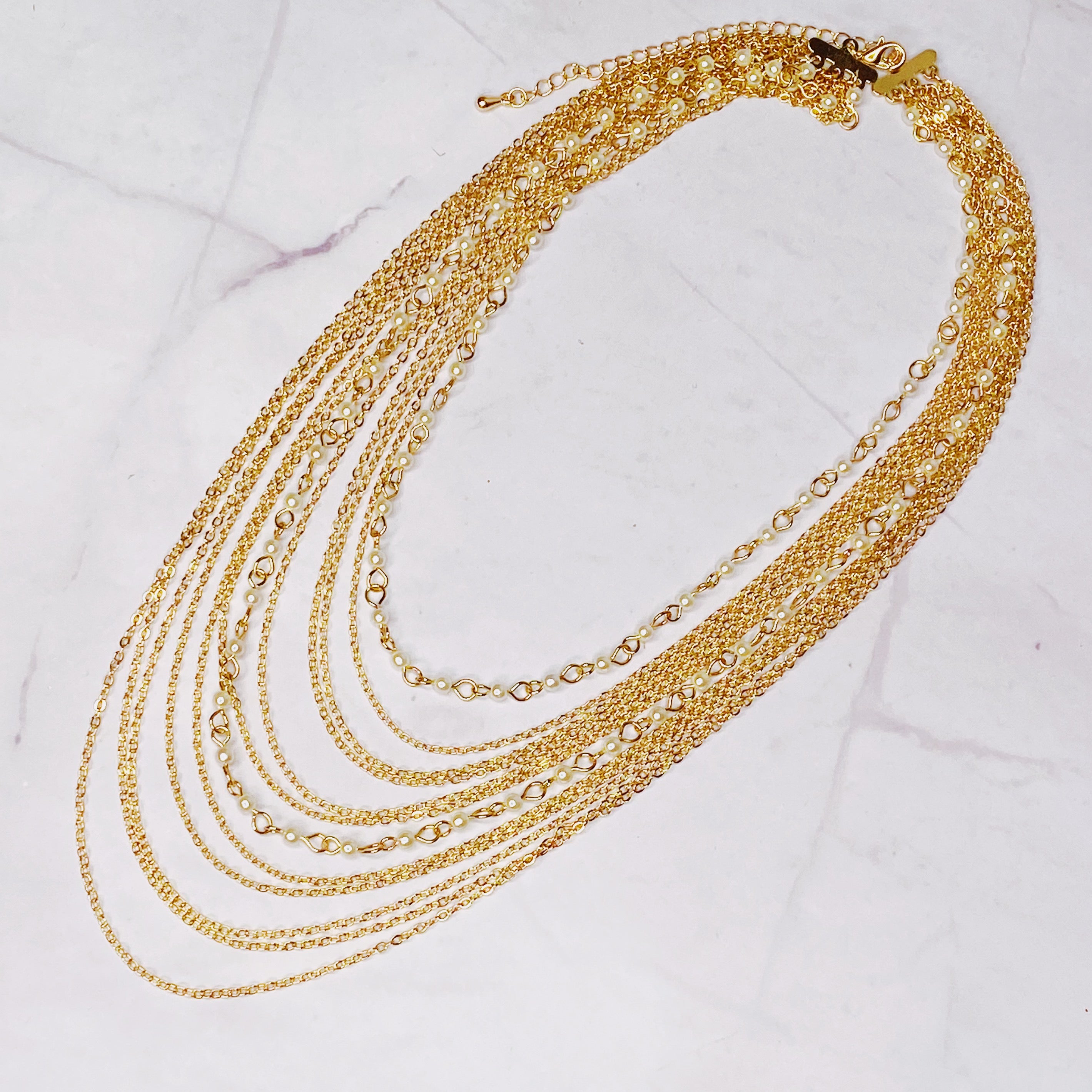 Beautifully Draping Pearl and Chain Necklace featuring 12 layers of gold plated chains and dainty acrylic pearls, elegantly draping around the neck.