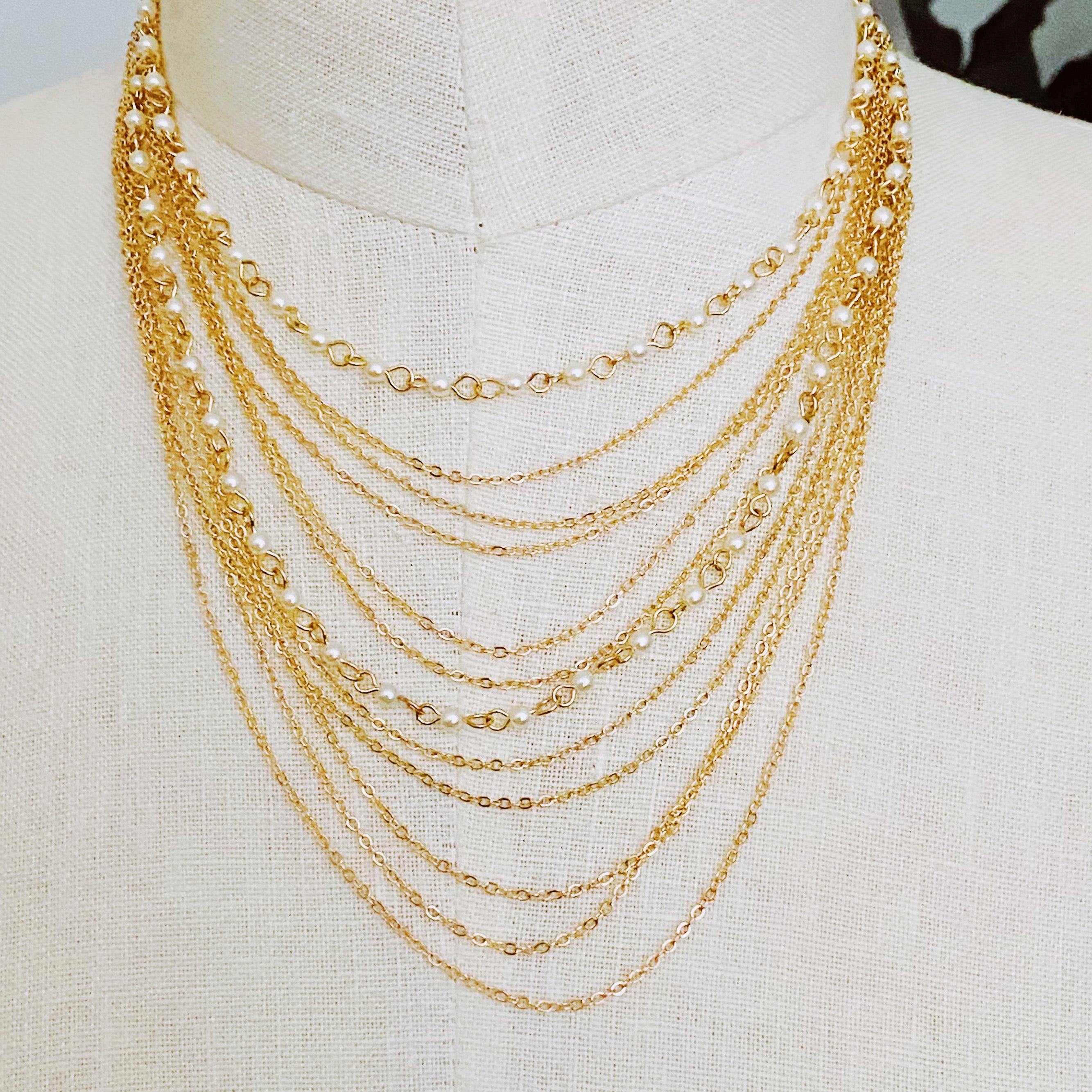 Beautifully Draping Pearl and Chain Necklace featuring 12 layers of gold plated chains and dainty acrylic pearls, elegantly draping around the neck.