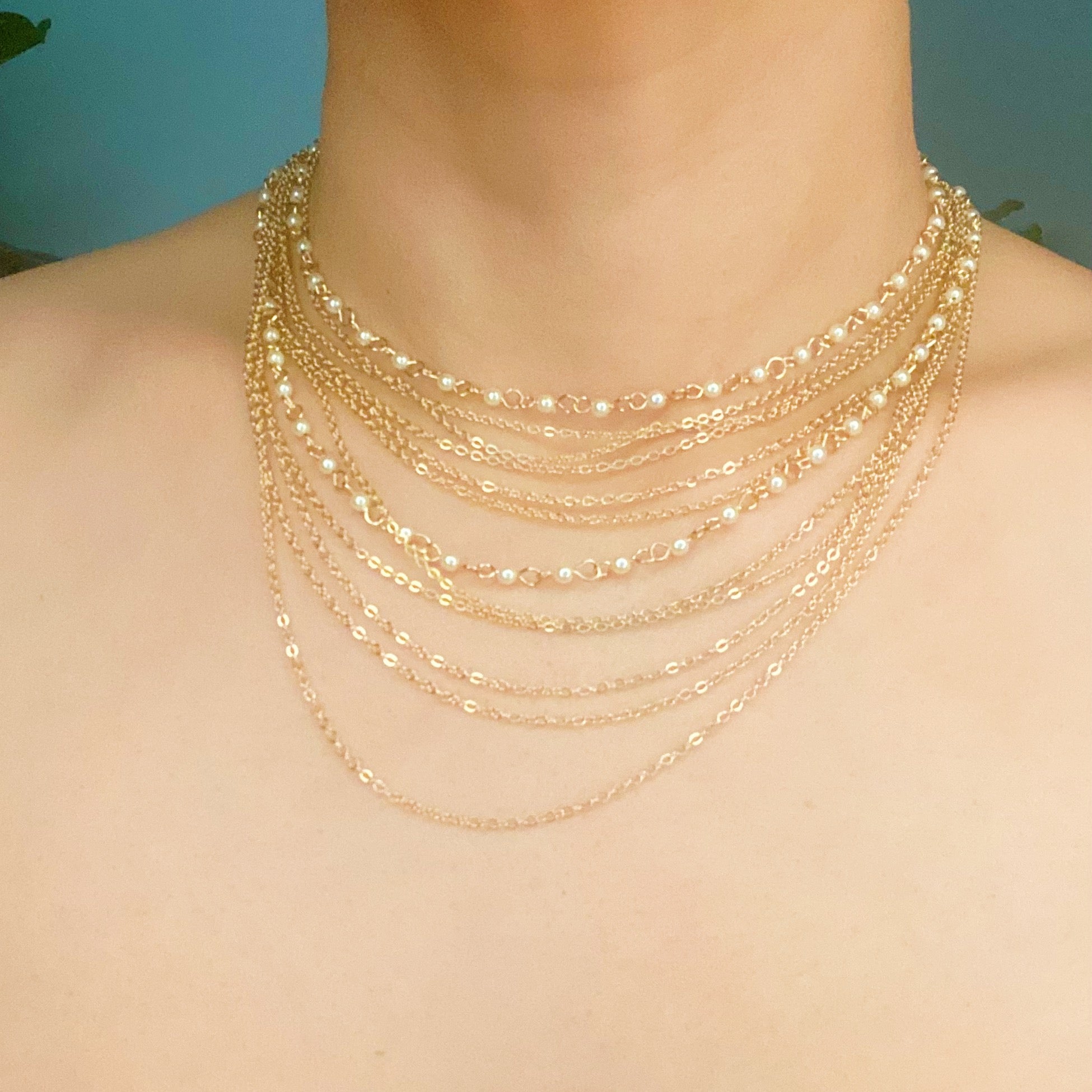 Beautifully Draping Pearl and Chain Necklace featuring 12 layers of gold plated chains and dainty acrylic pearls, elegantly draping around the neck.