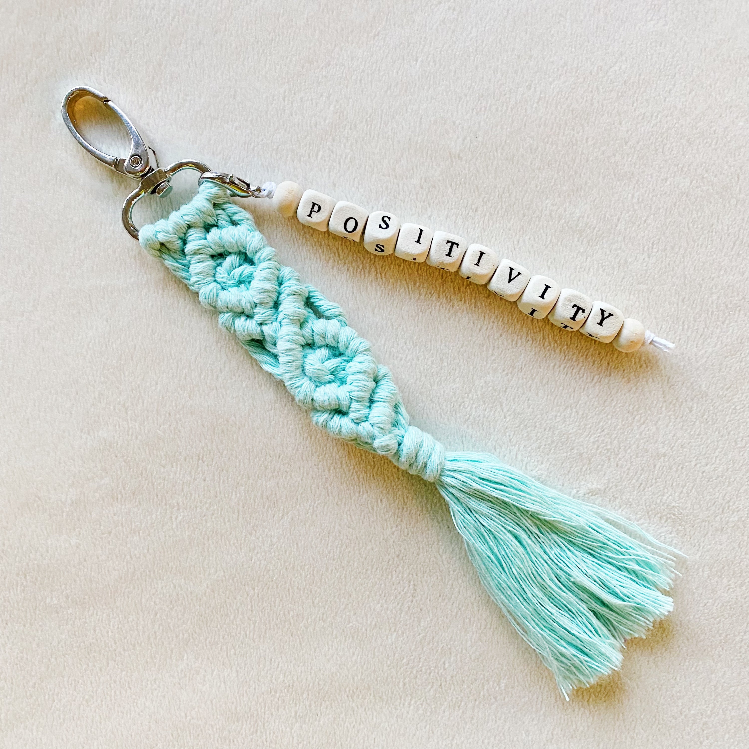 A stylish macrame braided key chain featuring empowering wooden cube beads, showcasing a bohemian design.