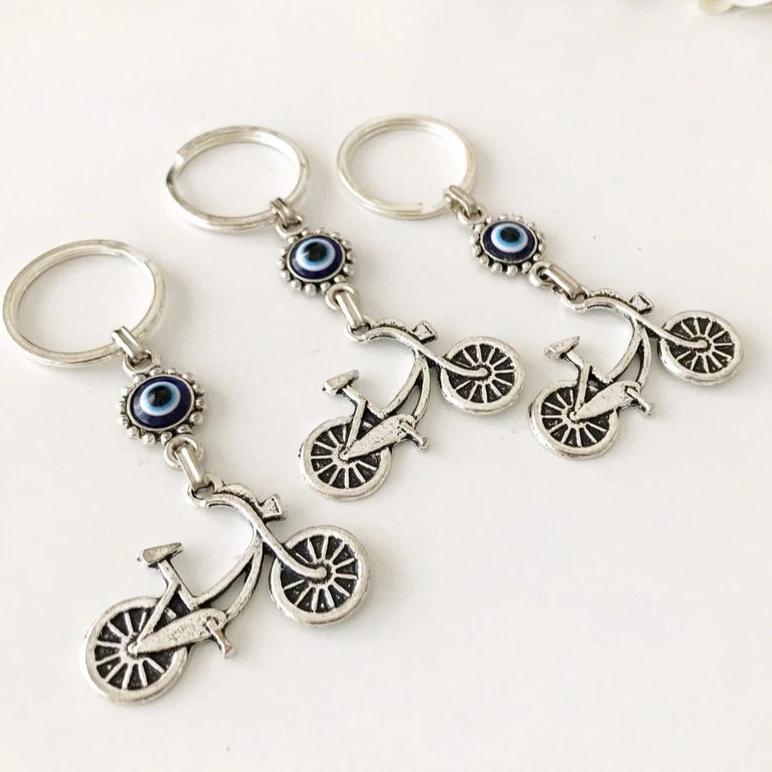 A silver bicycle keychain featuring a blue evil eye charm, symbolizing protection and luck.