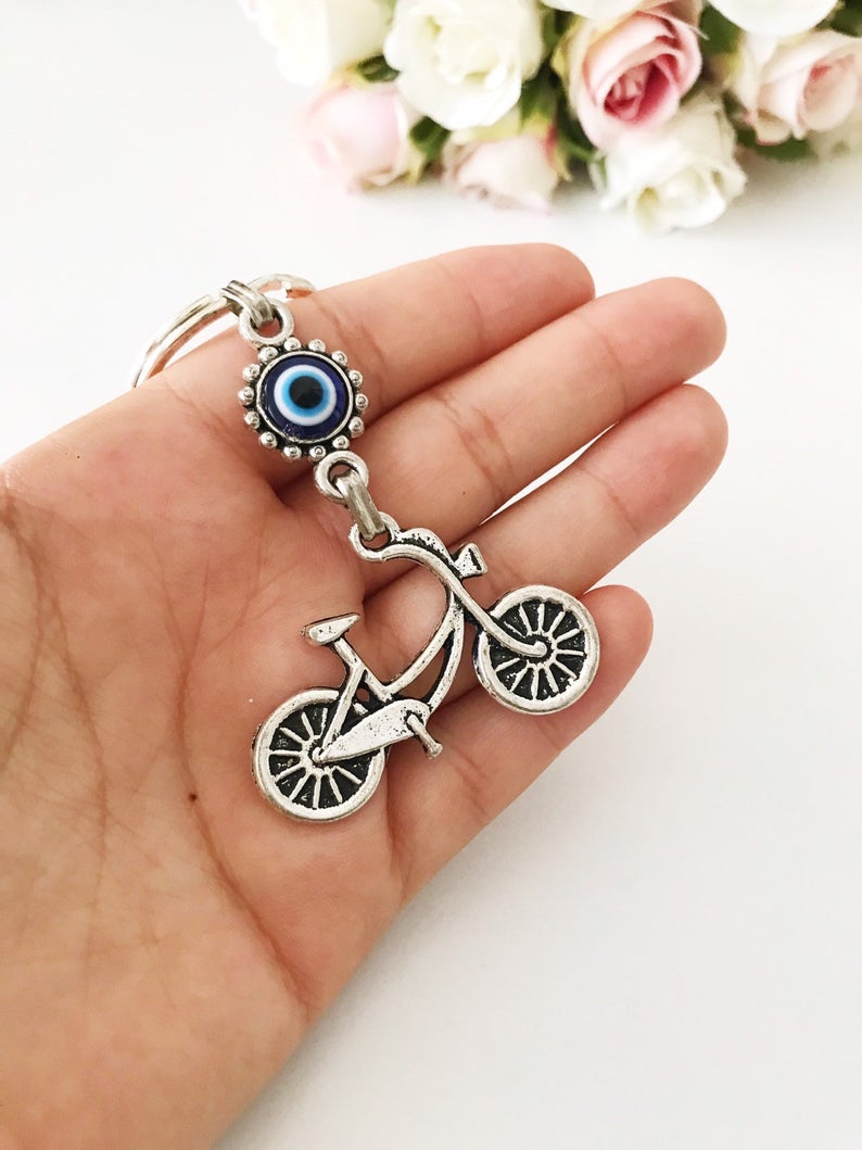 A silver bicycle keychain featuring a blue evil eye charm, symbolizing protection and luck.