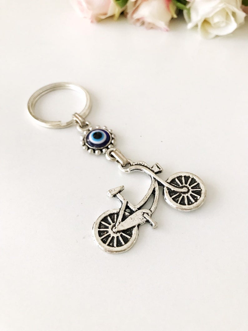 A silver bicycle keychain featuring a blue evil eye charm, symbolizing protection and luck.