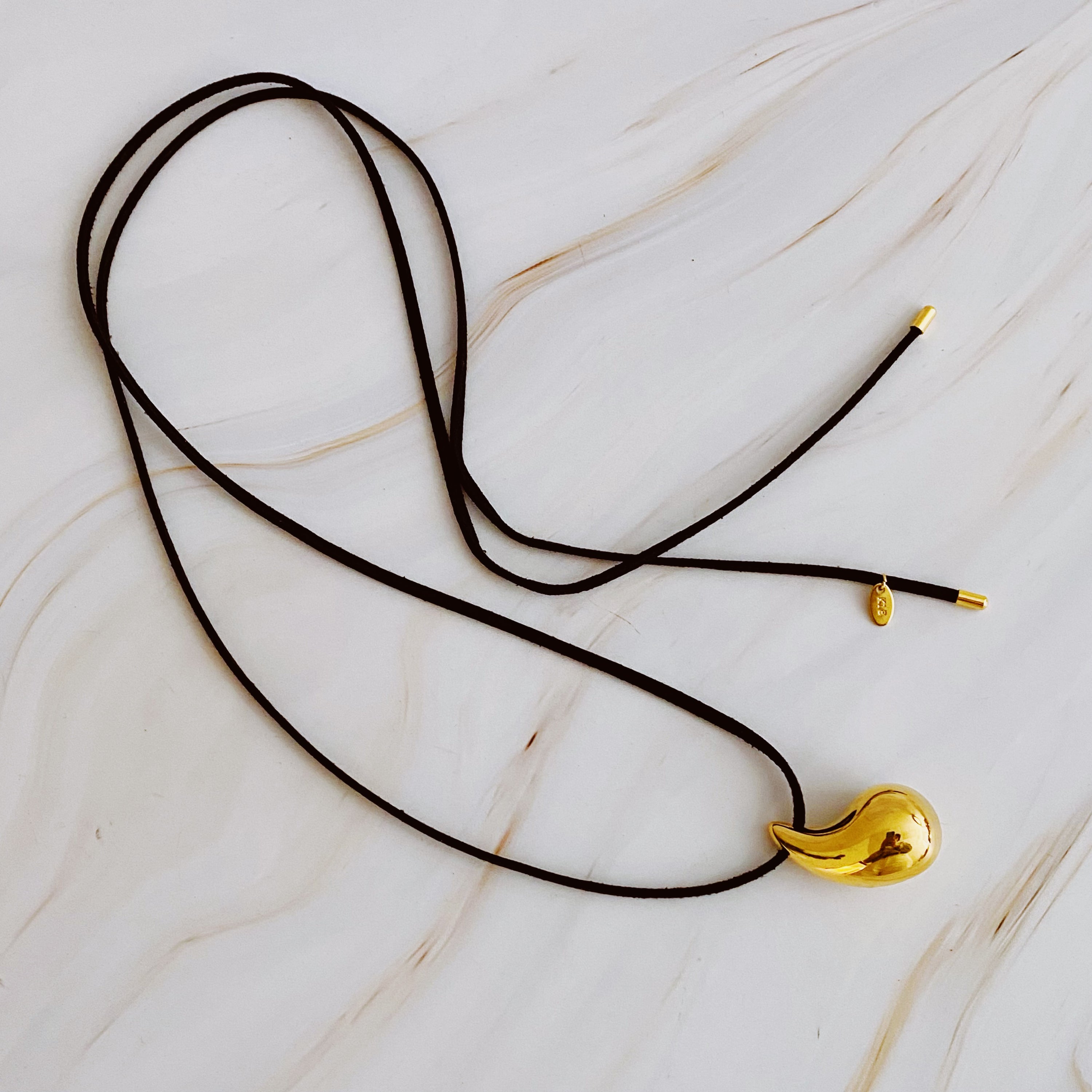 A stylish Black Leather Teardrop Necklace featuring a hollow teardrop pendant on a faux leather cord, elegantly displayed against a neutral background.