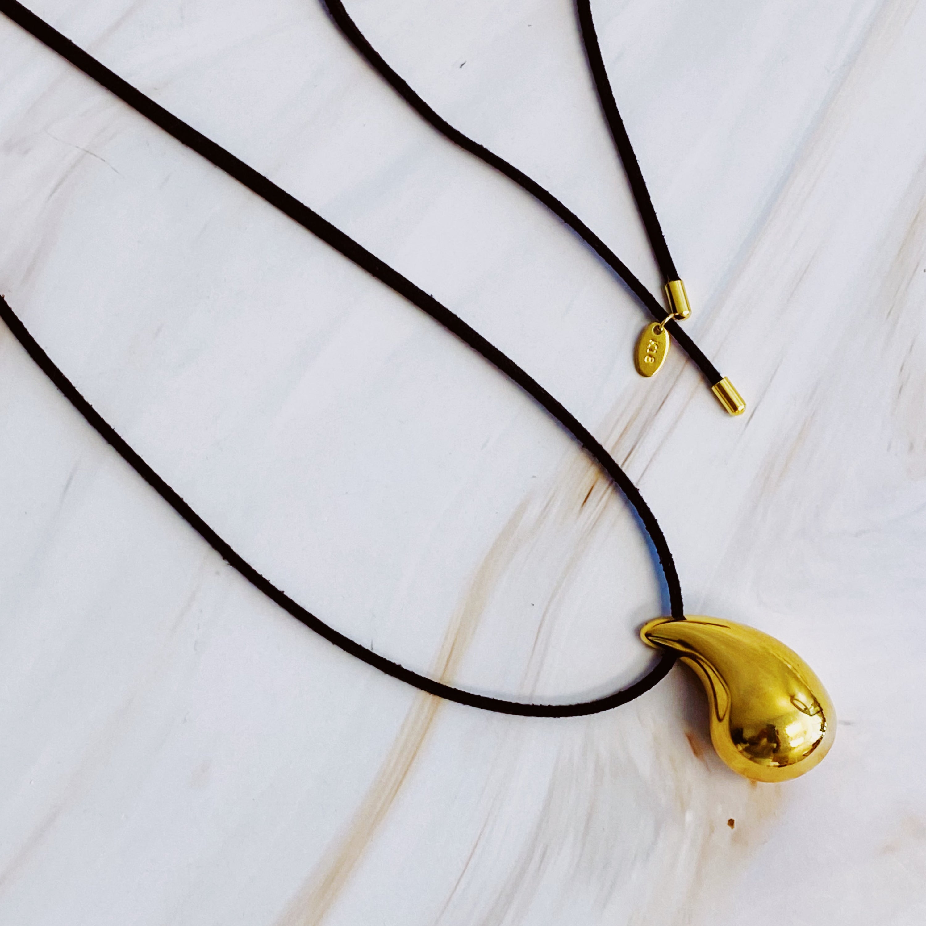 A stylish Black Leather Teardrop Necklace featuring a hollow teardrop pendant on a faux leather cord, elegantly displayed against a neutral background.