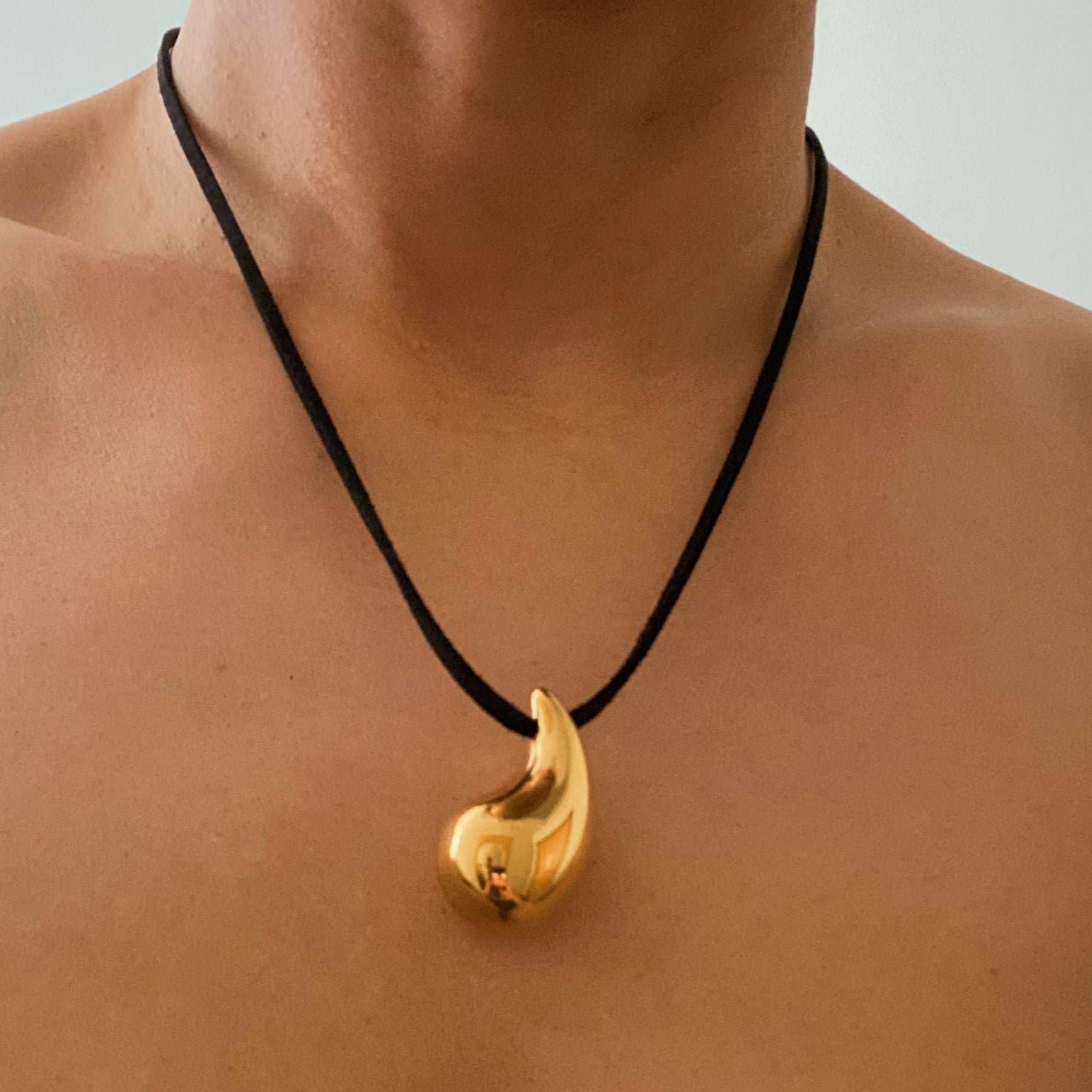 A stylish Black Leather Teardrop Necklace featuring a hollow teardrop pendant on a faux leather cord, elegantly displayed against a neutral background.