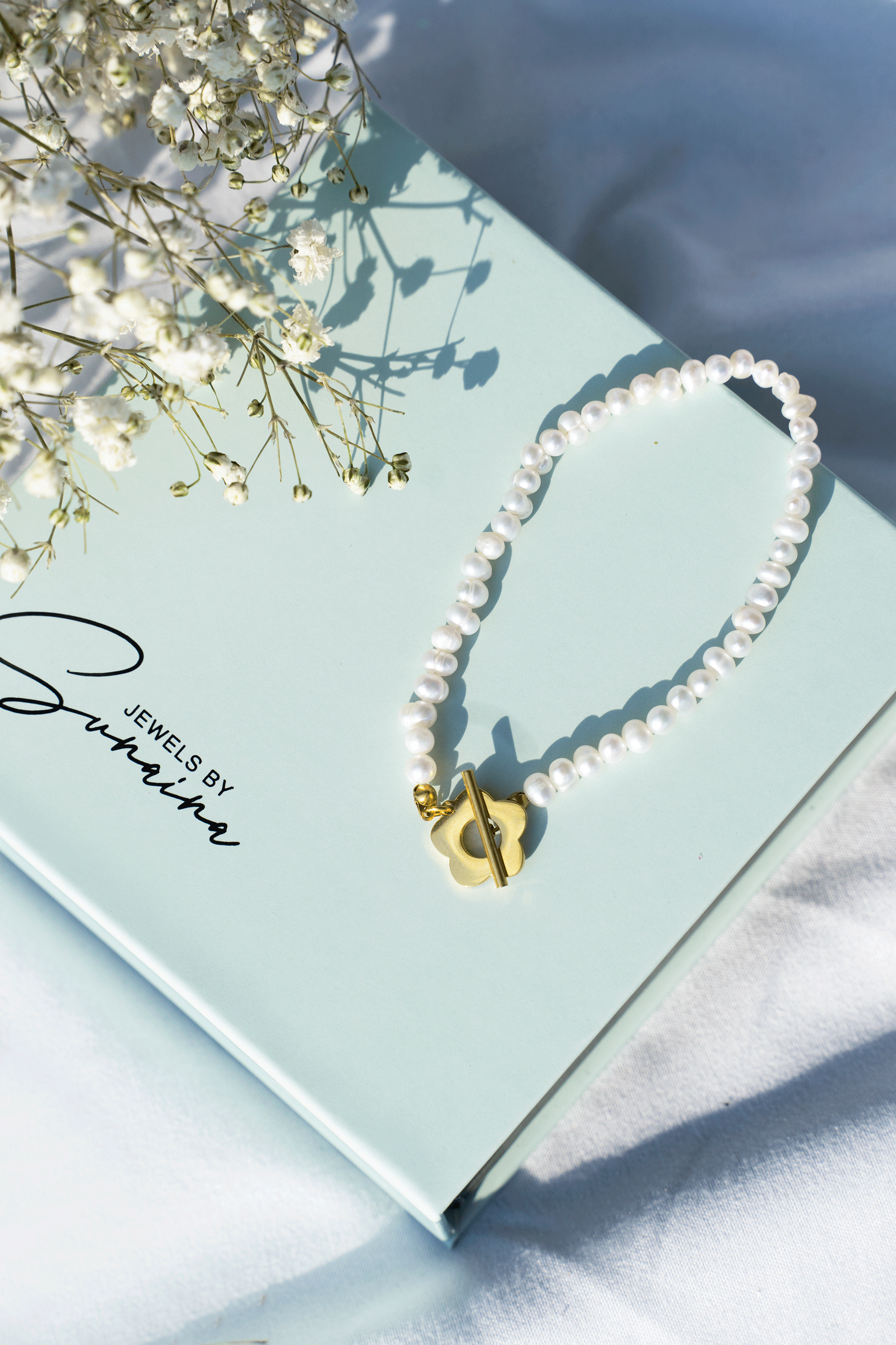 A stylish Blossom Bracelet featuring white freshwater pearls and an 18k gold plated blossom toggle clasp, elegantly displayed.