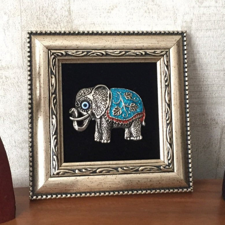 A beautifully framed wall decor featuring a silver elephant and a small evil eye bead, symbolizing luck and protection.