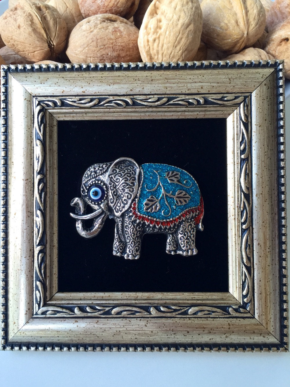 A beautifully framed wall decor featuring a silver elephant and a small evil eye bead, symbolizing luck and protection.