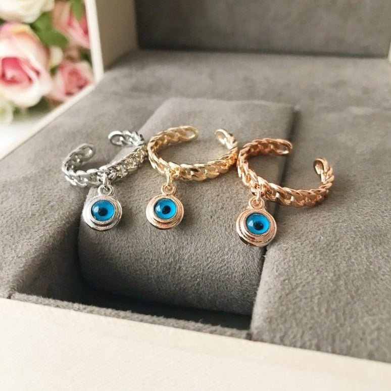 A stylish Blue Evil Eye Dangle Ring featuring a round blue evil eye bead, available in rose gold, silver, and gold finishes.