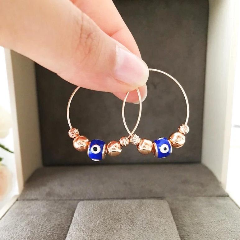 A pair of blue evil eye hoop earrings with a rose gold finish, featuring a small blue charm and a minimalist design.