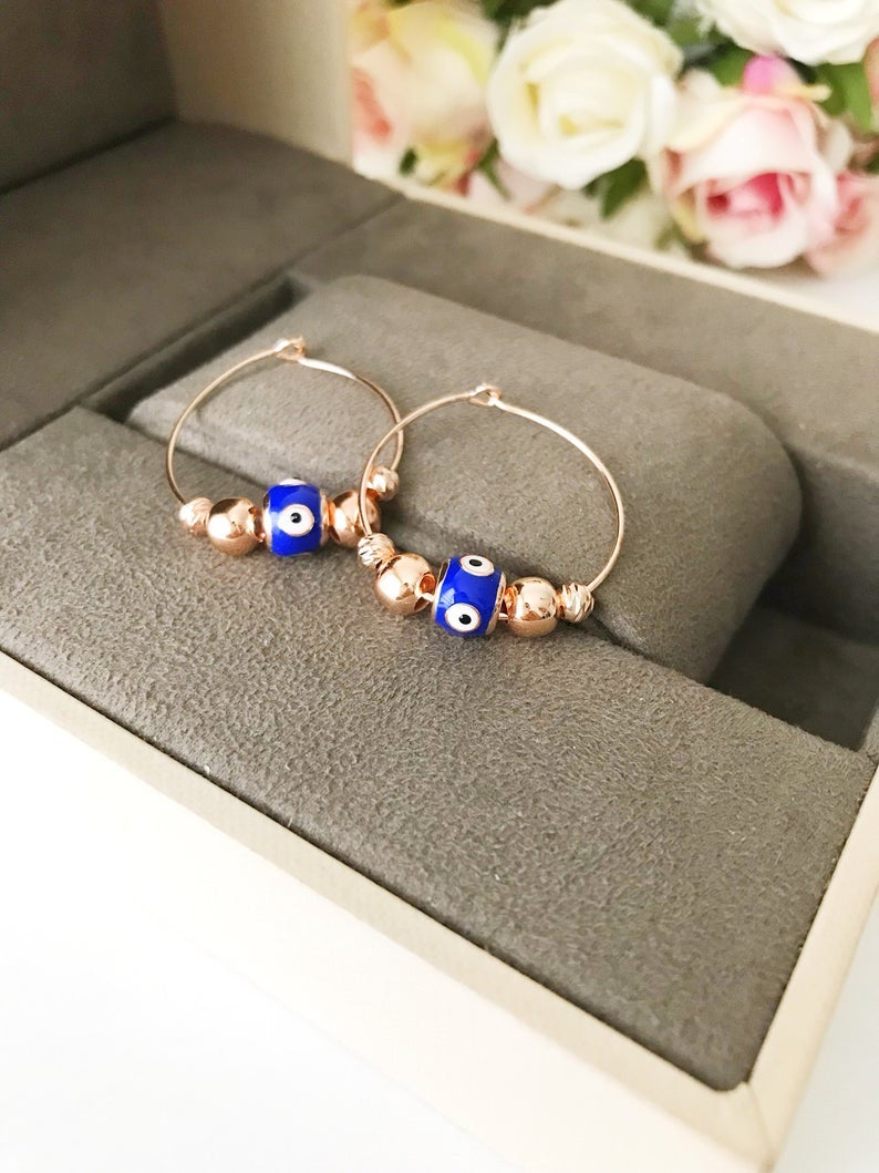 A pair of blue evil eye hoop earrings with a rose gold finish, featuring a small blue charm and a minimalist design.