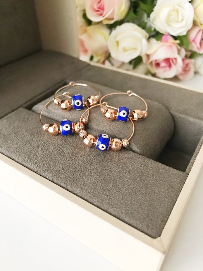 A pair of blue evil eye hoop earrings with a rose gold finish, featuring a small blue charm and a minimalist design.