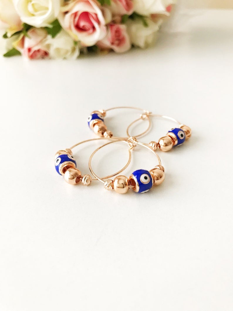 A pair of blue evil eye hoop earrings with a rose gold finish, featuring a small blue charm and a minimalist design.