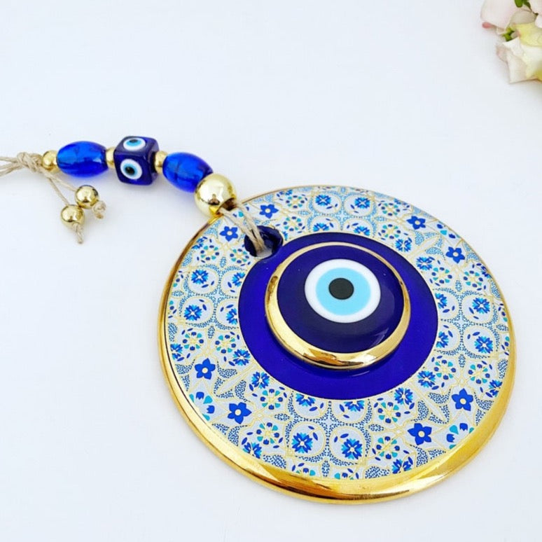 A beautiful Blue Evil Eye Wall Hanging featuring a 13cm blue centerpiece with a white patterned design and a gold evil eye bead.