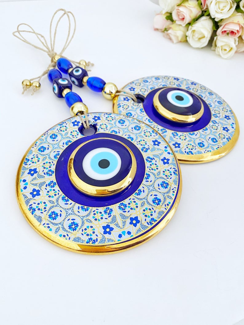 A beautiful Blue Evil Eye Wall Hanging featuring a 13cm blue centerpiece with a white patterned design and a gold evil eye bead.