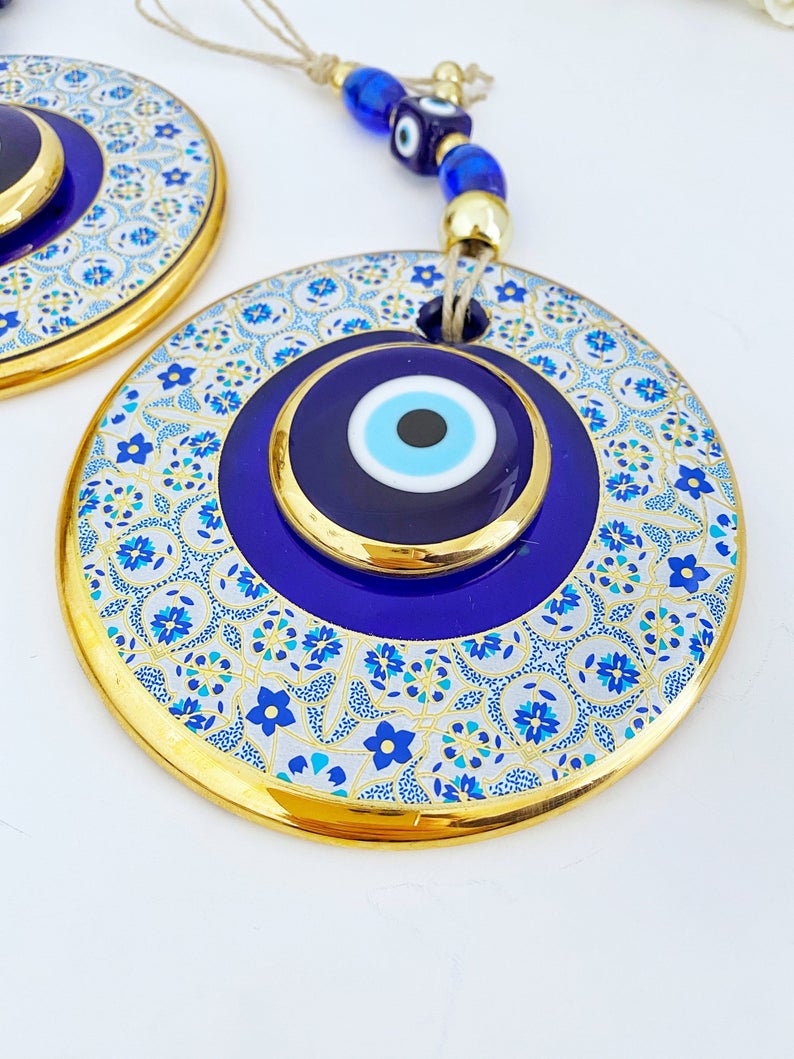 A beautiful Blue Evil Eye Wall Hanging featuring a 13cm blue centerpiece with a white patterned design and a gold evil eye bead.