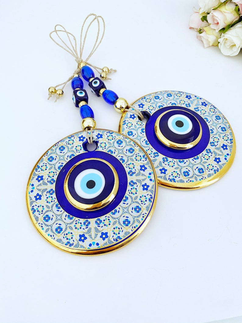 A beautiful Blue Evil Eye Wall Hanging featuring a 13cm blue centerpiece with a white patterned design and a gold evil eye bead.