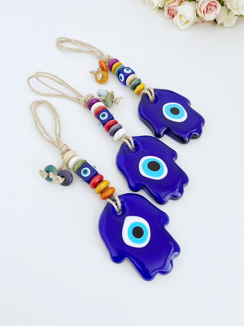 A beautiful Blue Evil Eye Wall Hanging featuring a handmade glass Hamsa design, showcasing intricate macrame details and vibrant colors.