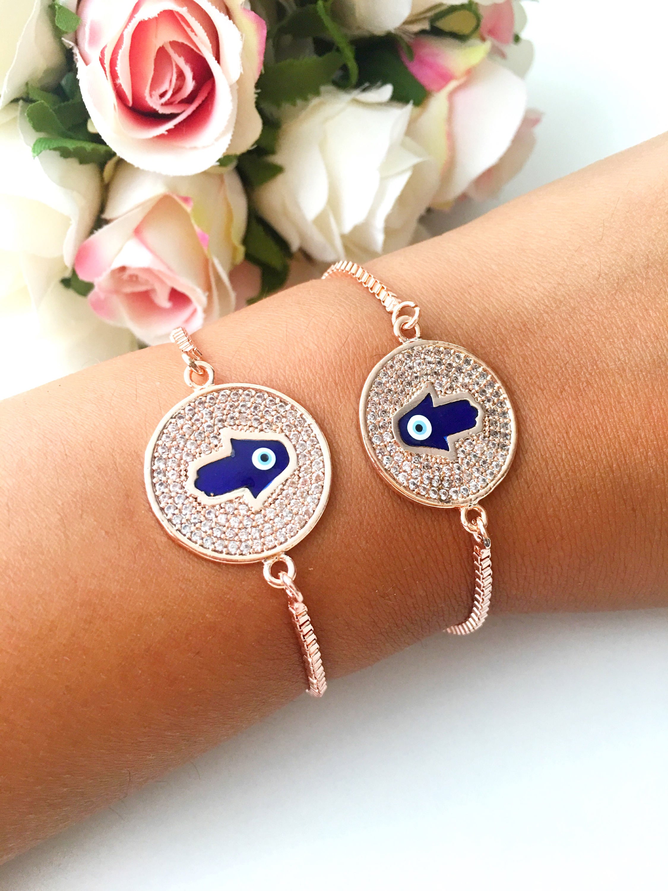 A beautiful Blue Hamsa Evil Eye Bracelet featuring a blue evil eye charm and a rose gold stainless steel disc, adjustable for a perfect fit.