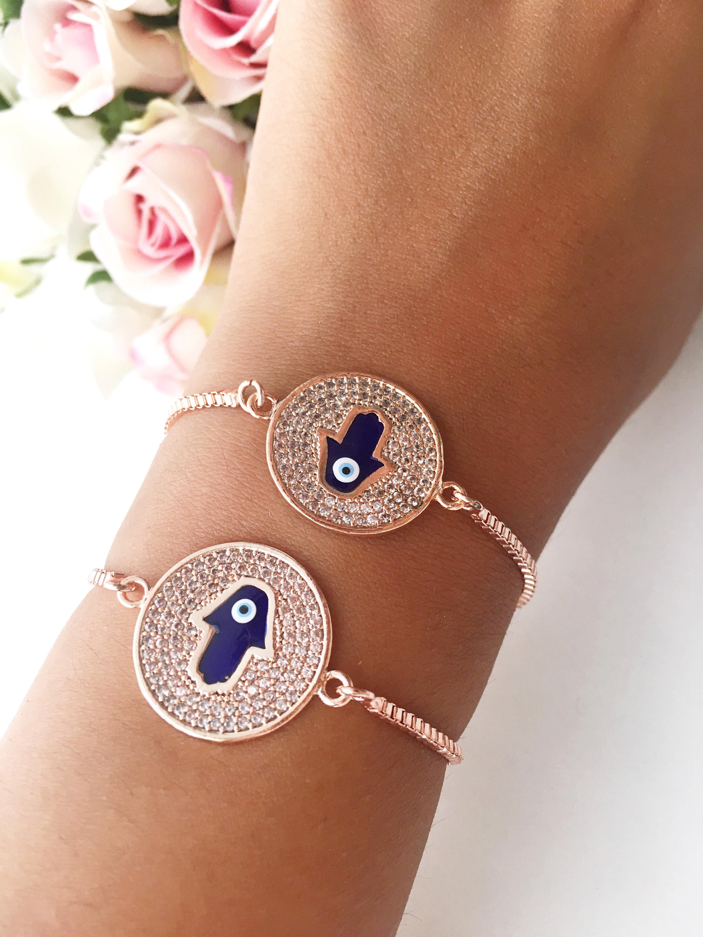 A beautiful Blue Hamsa Evil Eye Bracelet featuring a blue evil eye charm and a rose gold stainless steel disc, adjustable for a perfect fit.