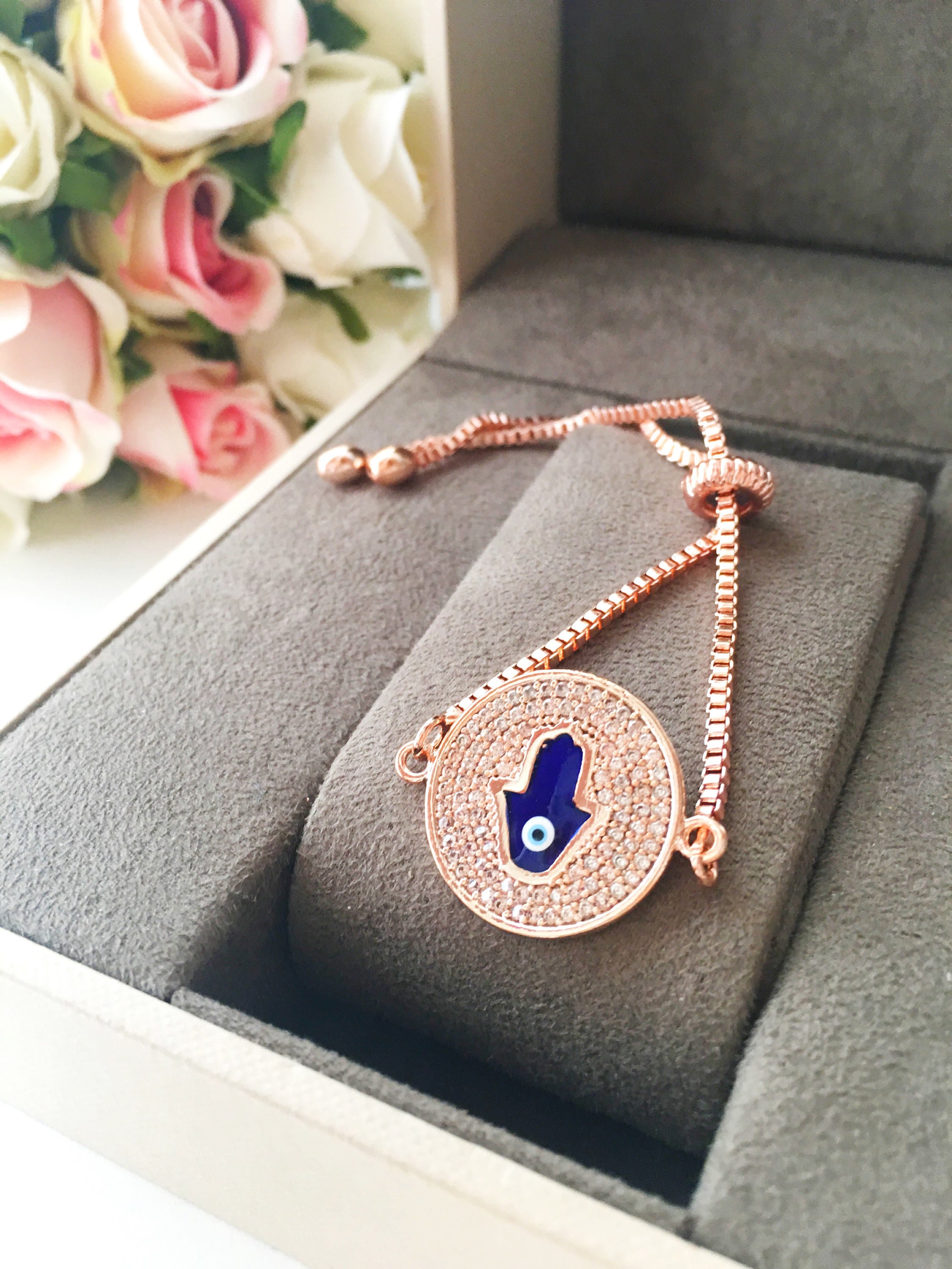 A beautiful Blue Hamsa Evil Eye Bracelet featuring a blue evil eye charm and a rose gold stainless steel disc, adjustable for a perfect fit.