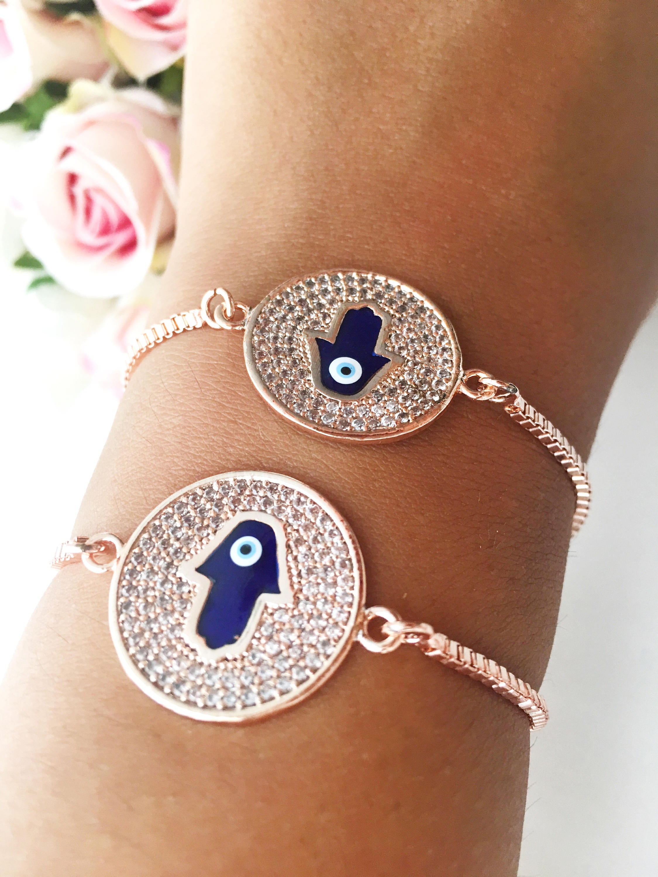 A beautiful Blue Hamsa Evil Eye Bracelet featuring a blue evil eye charm and a rose gold stainless steel disc, adjustable for a perfect fit.