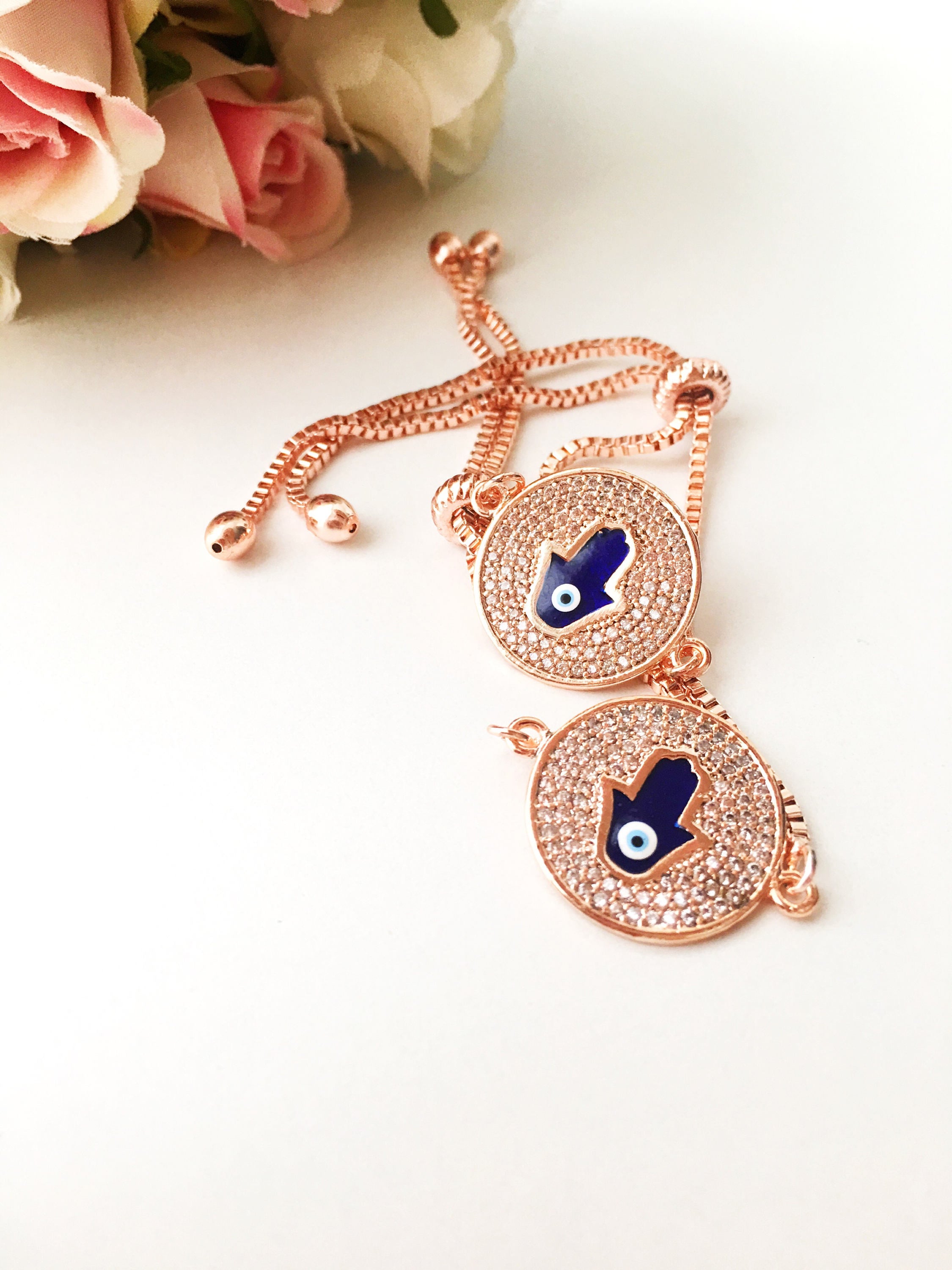 A beautiful Blue Hamsa Evil Eye Bracelet featuring a blue evil eye charm and a rose gold stainless steel disc, adjustable for a perfect fit.