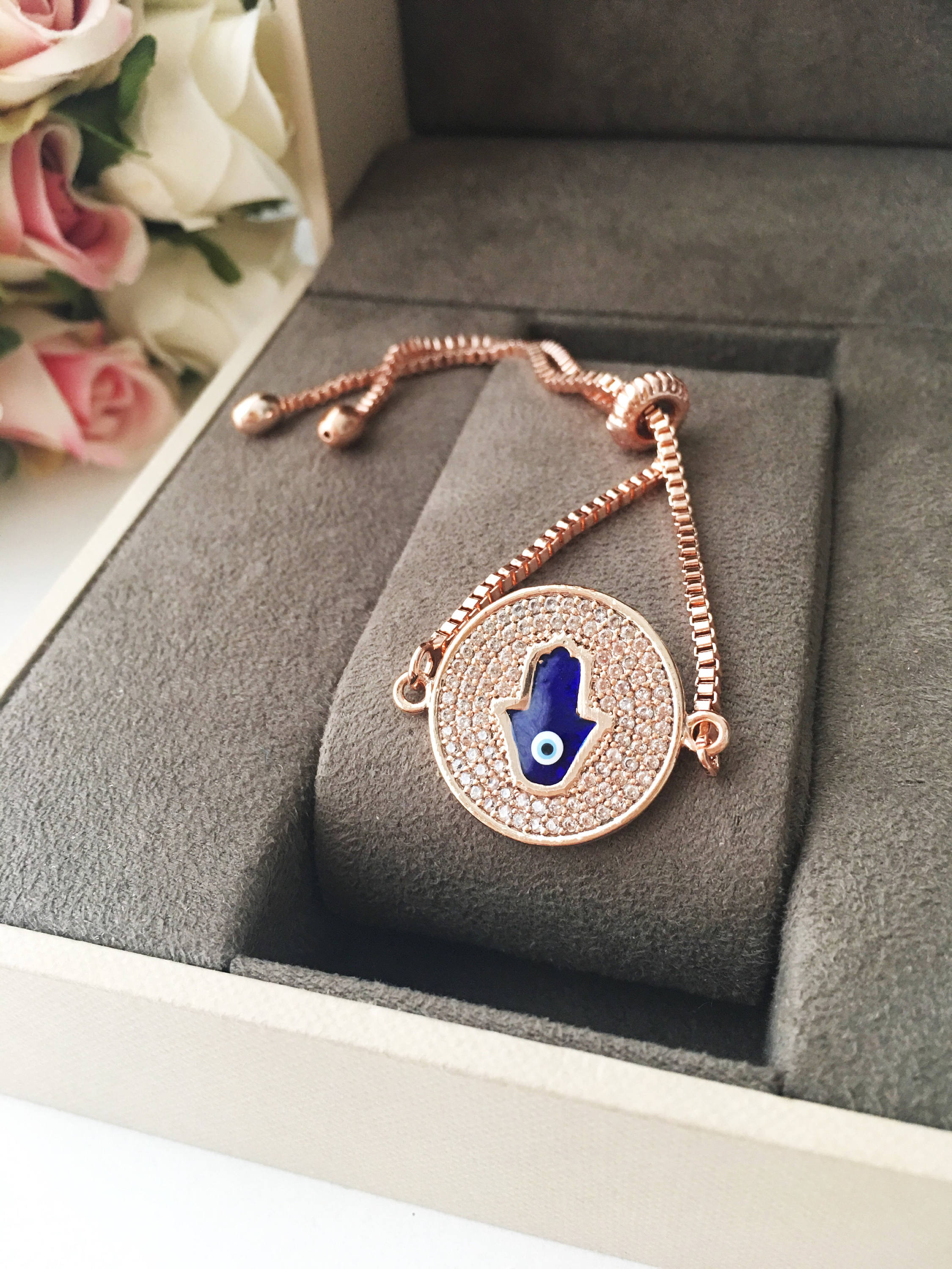 A beautiful Blue Hamsa Evil Eye Bracelet featuring a blue evil eye charm and a rose gold stainless steel disc, adjustable for a perfect fit.