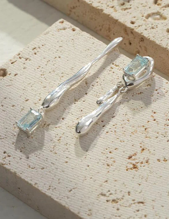 Handmade blue topaz drop earrings in sterling silver, showcasing unique gemstone qualities and artistic design.