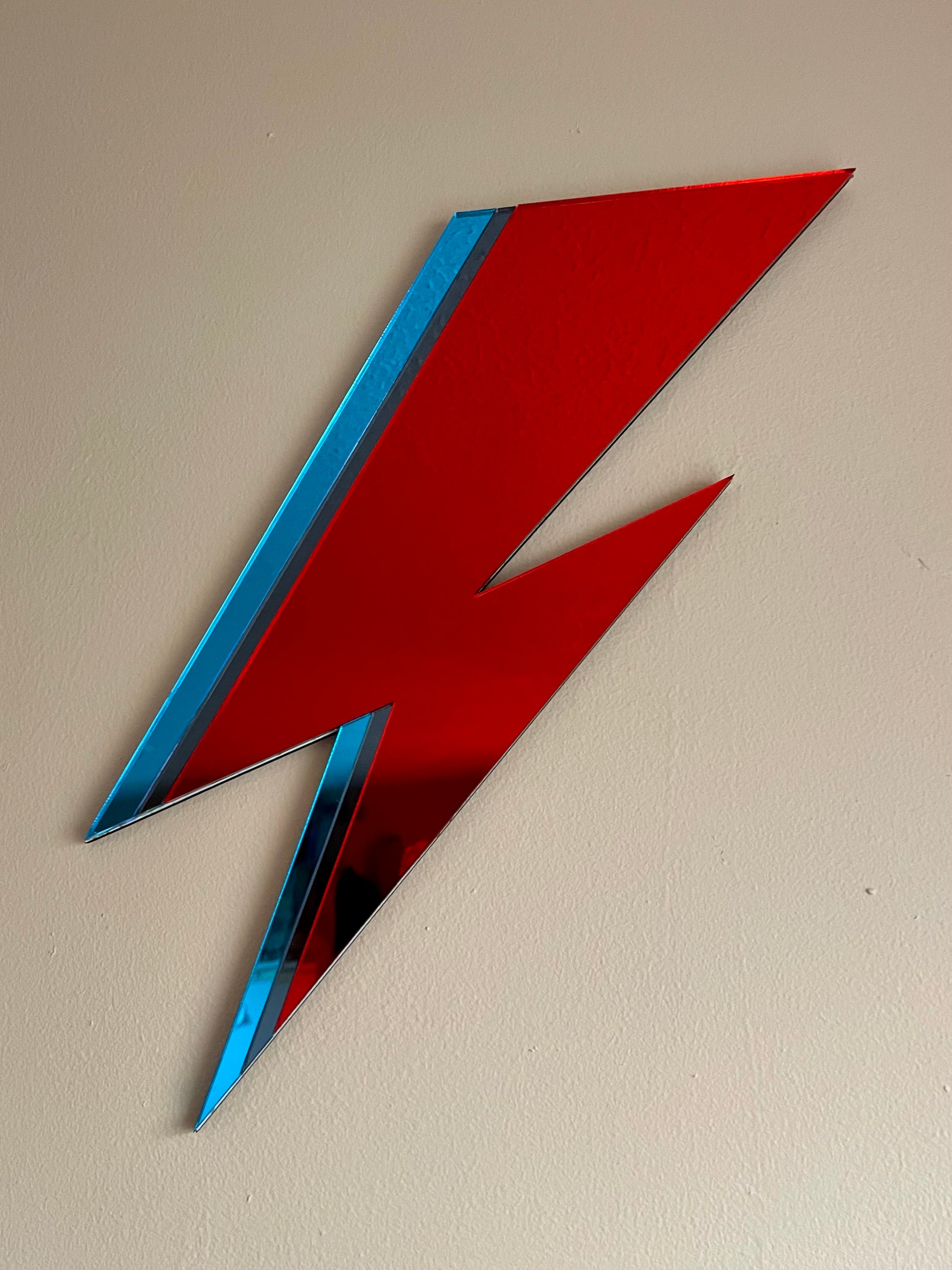 A vibrant Bolt Mirror Wall Hanging featuring red, pewter, and blue acrylic in a stylish design, perfect for home decor.