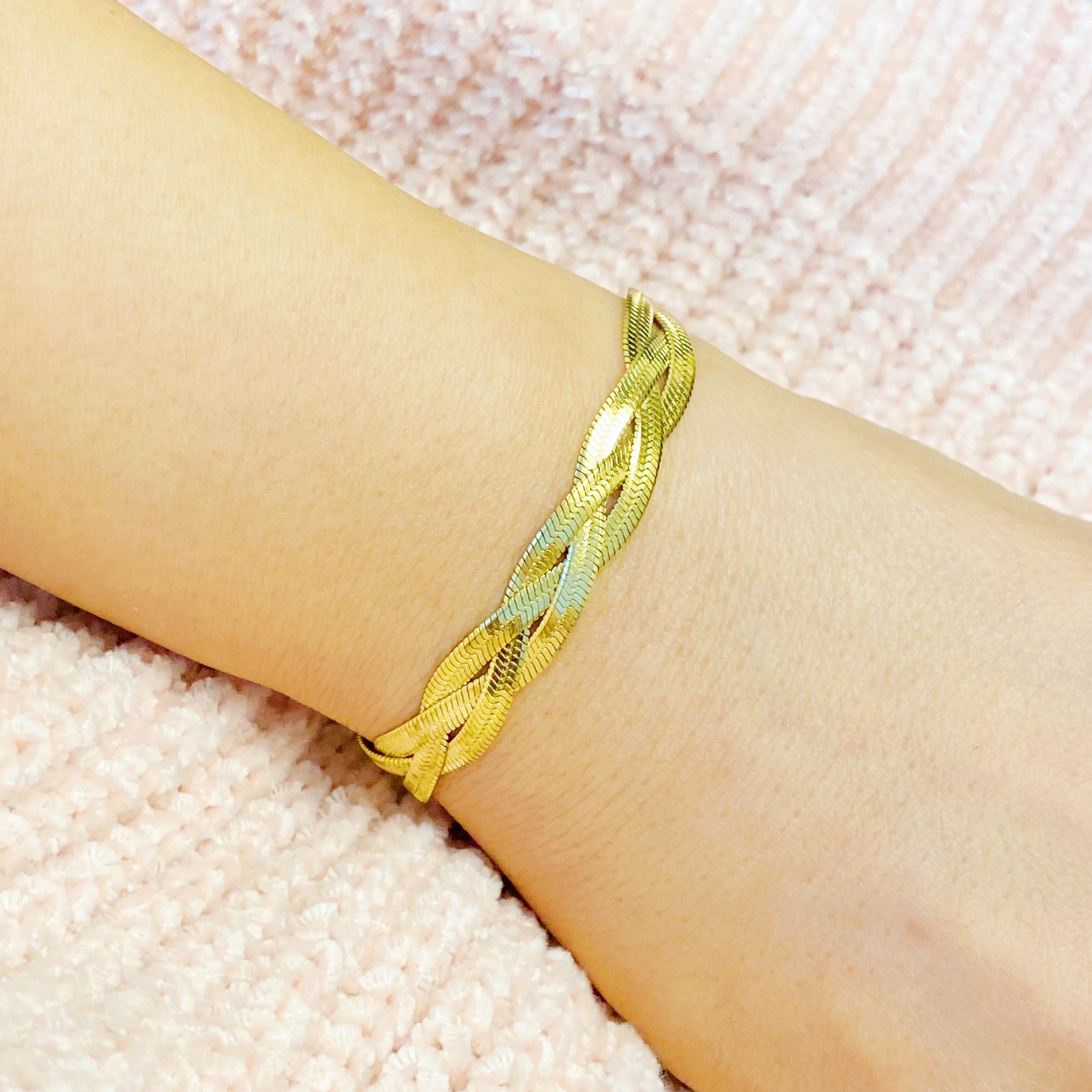 A close-up of a gold plated braided herringbone chain bracelet, showcasing its intricate design and shiny finish.