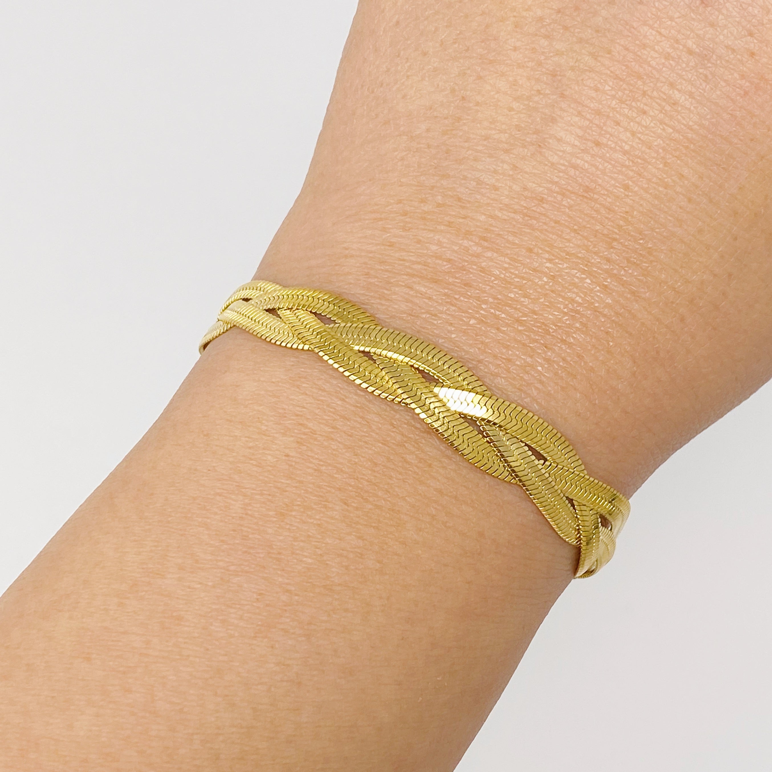 A close-up of a gold plated braided herringbone chain bracelet, showcasing its intricate design and shiny finish.