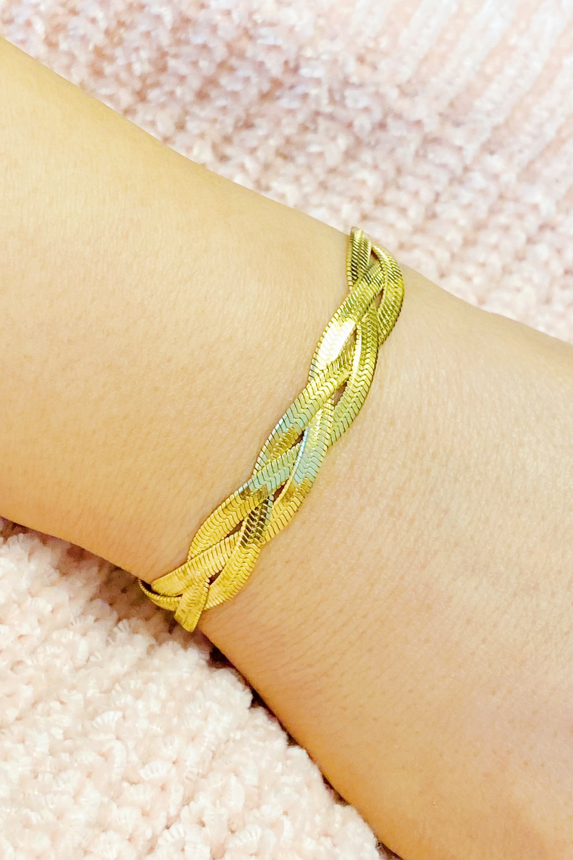 A close-up of a gold plated braided herringbone chain bracelet, showcasing its intricate design and shiny finish.