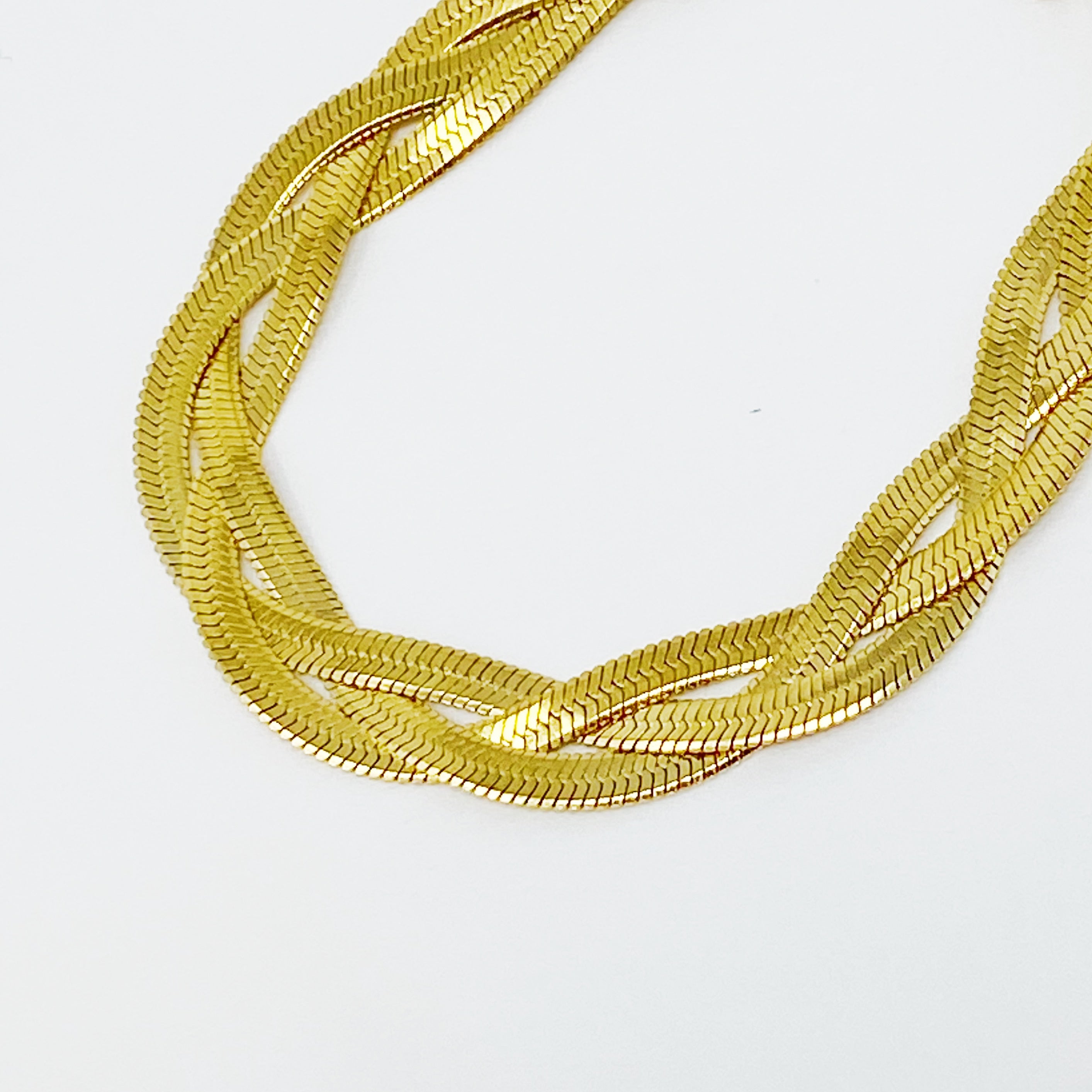 A close-up of a gold plated braided herringbone chain bracelet, showcasing its intricate design and shiny finish.