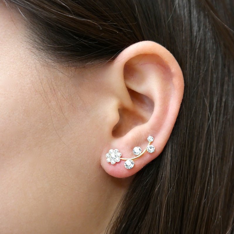 A pair of handmade brass flower ear cuffs and climber earrings in gold, featuring white CZ crystals, elegantly displayed on a soft background.